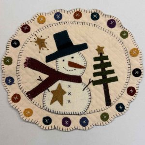 Simone wool applique table mat kit featuring primitive snowman with top hat, maroon scarf, golden star accent, evergreen tree, and hand-stitched penny circle border on cream wool background