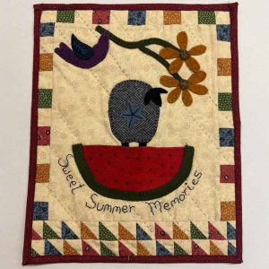 Sweet Summer wool applique wall hanging kit featuring folk art crow on watermelon, purple bird, rust-colored daisies, and patchwork border with triangle piecing on cream background with embroidered text
