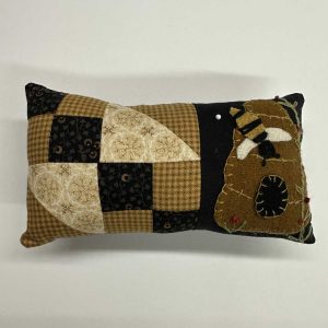 Decorative patchwork pin cushion featuring a quilted pattern in brown, black and cream fabrics, with an appliqued folk art bee design on the right side