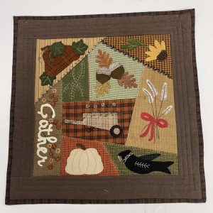 Autumn wool applique wall hanging with brown border showcasing seasonal motifs in textured wools including acorns, leaves, wheat with red bow, black crow, white pumpkin, and 'October' text