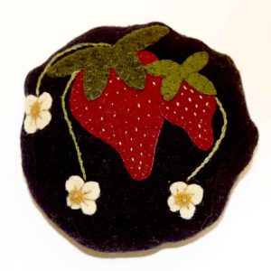 Circular wool pin cushion in dark purple featuring red strawberries with embroidered seeds, green leaves, and three cream-colored strawberry blossoms with yellow centers
