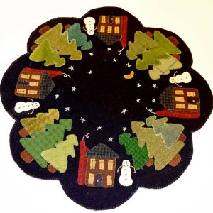 Scalloped wool penny rug in black featuring winter village scene with five red saltbox houses, evergreen trees in varied green wools, white snowmen, and embroidered stars against night sky with yellow moon